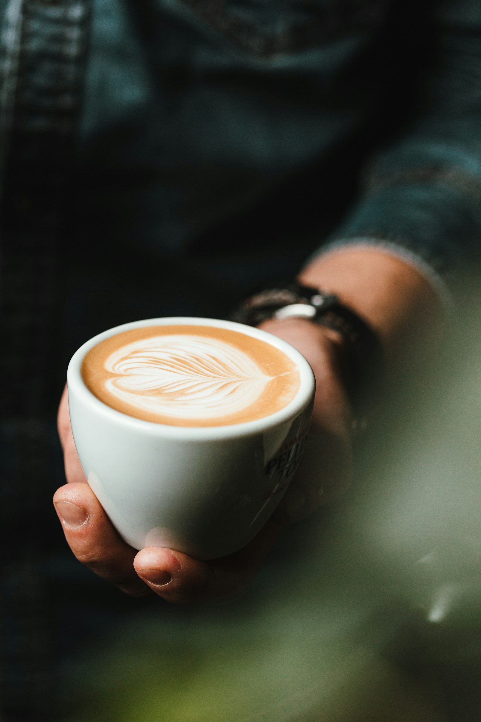Hand holding a ceramic cup of café latte with rosetta latte art